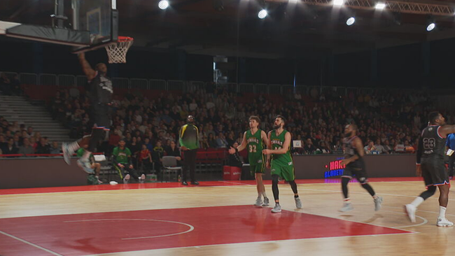 Basketball-Feld mit Spielern drauf während eines Spiels. Ein Spieler ist gerade im Sprung um den Ball in den Korb zu werfen.