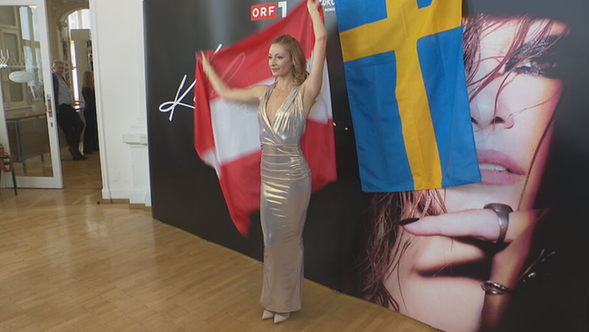 Kaleen hält Österreich-Flagge hinter ihrem Rücken hoch und lächelt zu den Fotografen