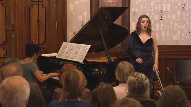 Sängerin steht neben Klavier in einem voll besetzten Saal