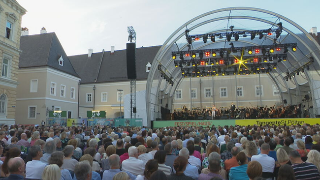 Domplatz in St. Pölten mit bespielter Bühne und sitzendem Publikum davor.