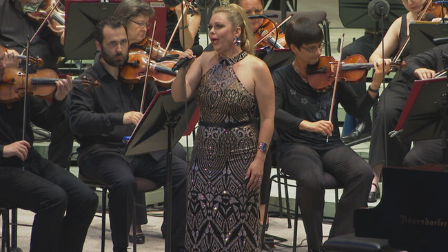 © ORF / Seitenblicke Daniela Fally, in schönem Abendkleid, singend mit Mikrofon in der Hand vor Orchester stehend