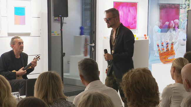 © ORF / Seitenblicke Hochmair in Aktion, mit Mikrofon, Sonnebrille - auf dem Weg zur Bühne in einer Galerie