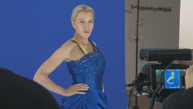 Heather Mills in blauem Kleid vor blauer Wand schaut in Kamera