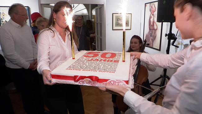 Kellnerinnen tragen eine große Torte mit Kerzen in die Galerie. Darauf steht "50 Jahre Galerie Martin Suppan".