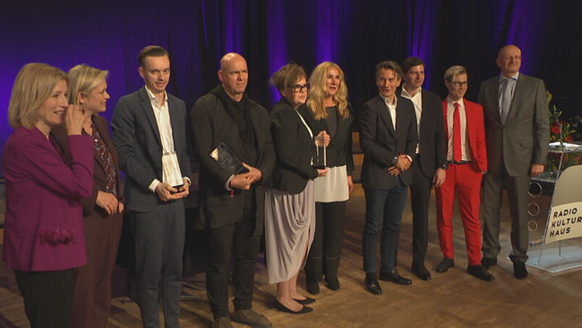 © ORF / Seitenblicke Gruppe, teilweise mit Trophäen in den Händen, steht auf einer Bühne und wird fotografiert.