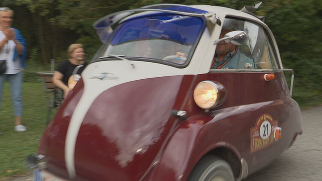 © ORF / Seitenblicke Kleiner dunkelroter Oldtimer mit 2 Sitzen fährt vorbei