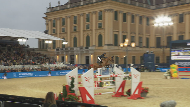 Pferd mit Reiter springt über Hürde, dahinter Schloss Schönbrunn