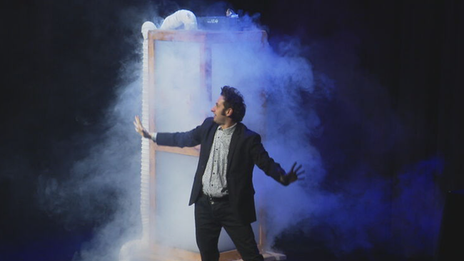 Magier steht auf Bühne, dahinter ein Menschen-großer Glas-Kasten voller Nebel