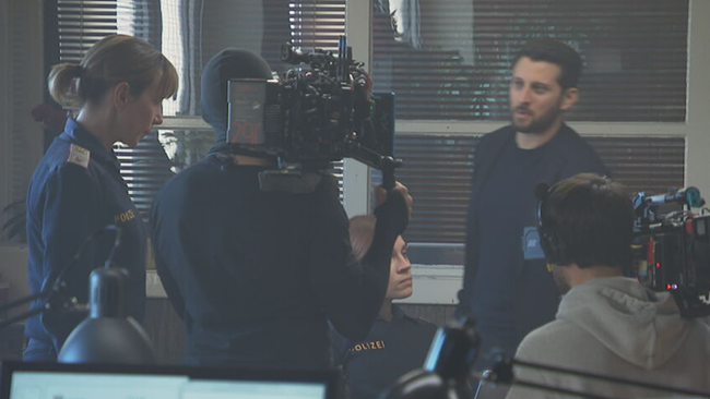 © ORF / Seitenblicke Schauspielerin Julia Koschitz steht als Polizisten im Revier, mit KollegInnen und filmender Crew
