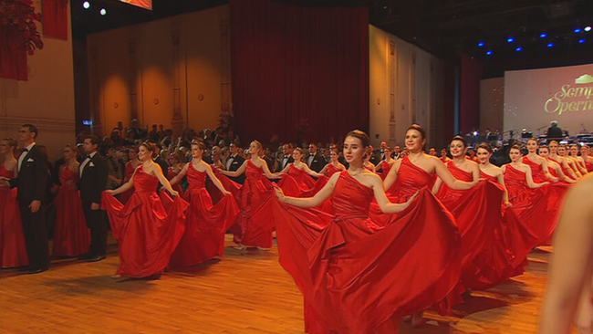 Debütanten Paare ziehen ein und die Damen schwingen die Röcke ihrer roten Kleider dabei