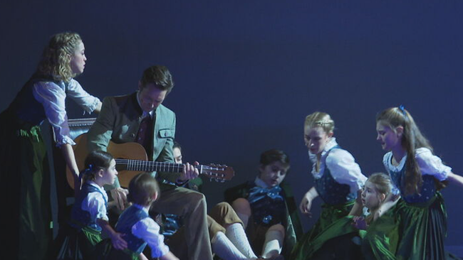 Lukas Perman als Kapitän von Trapp sitzt auf der Bühne umgeben von seiner Musical-Familie