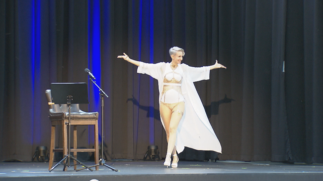 Lisa Eckhart betritt in weißem Kostüm mit weit ausgebreiteten Armen die Bühne