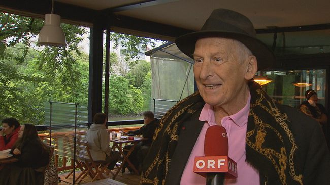 Erich Schleyer lachend mit Hut und bunt gekleidet im Interview auf der Summerstage