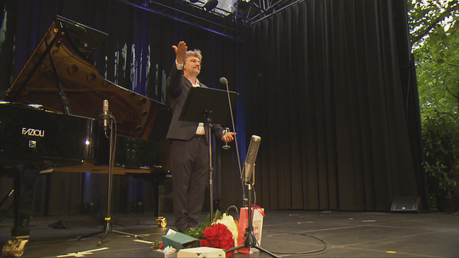 Jonas Kaufmann mit dankend ausgestreckter Hand und Geschenken vor den Füßen auf der Bühne