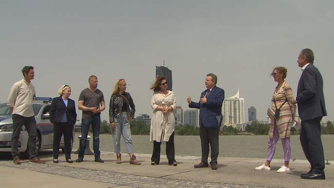 Das Team hinter Soko Donau und Bürgermeister stehen im Halbkreis vor der Donau mit Skyline im Hintergrund