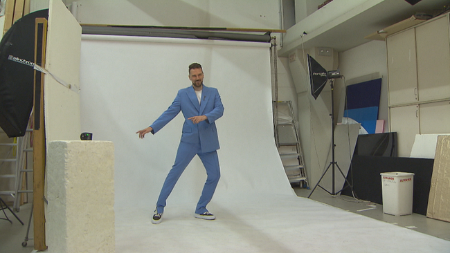 Designer Niko Niko tanz im blauen Anzug vor weißer Leinwand beim Shooting