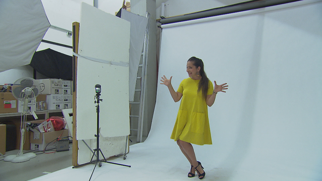 Caroline Athanasiadis posiert in gelben Kleid vor weißer Leinwand mit "Jazz Hands"