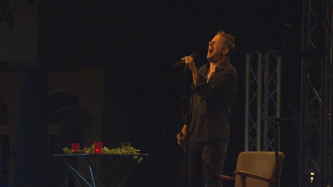 Philipp Hochmair schreit leidend auf der Bühne ins Mikrofon mit einer Flasche in der Hand