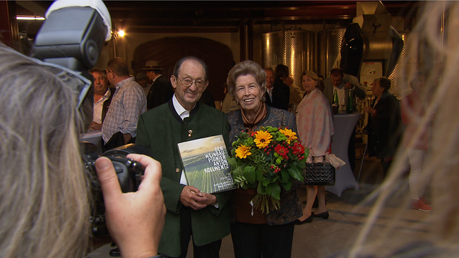 Winzer Anton und Senior-Chefin Margarete Kollwentz posieren mit einem neuen Buch und Blumenstrauß