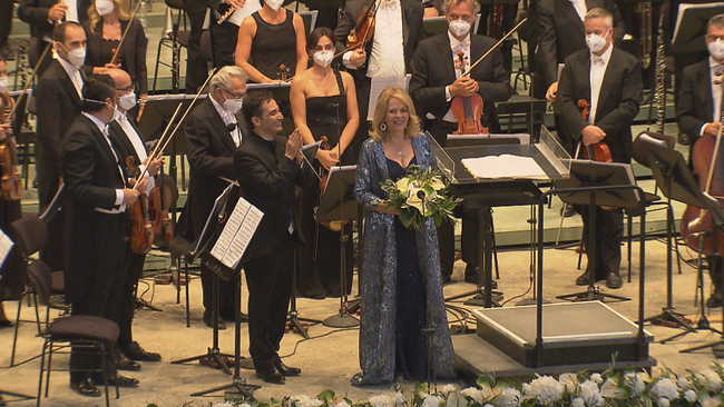 Renée Fleming auf der Bühne beim Schlussapplaus mit Blumenstrauß in der Hand und umringt vom Orchester