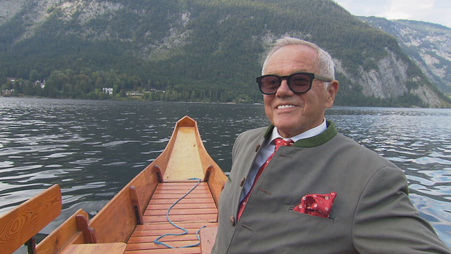 Wolfgang Puck im Interview auf einem Holzboot am See, im Hintergrund die Berge