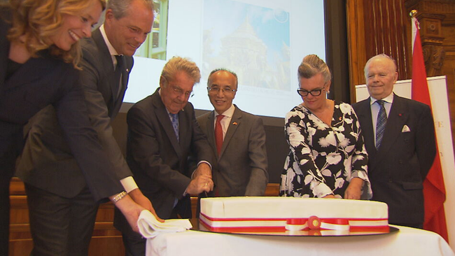 VertreterInnen des österreichisch-chinesischeen Austauschs schneiden großen Kuchen mit rot-weiß-rot Fahne an 