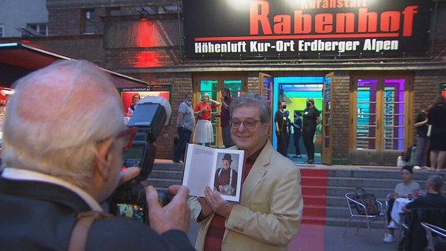 Steinhauer posiert mit aufgeschlagenem Buch für Fotografen vor dem Rabenhof 