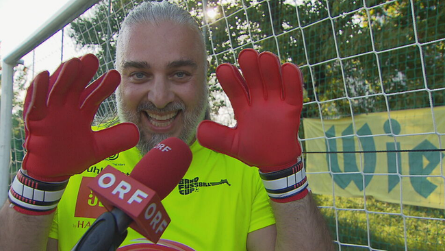 Georgij Makazaria lacht in die Kamera, die Hände in roten Torhüter-Handschuhen