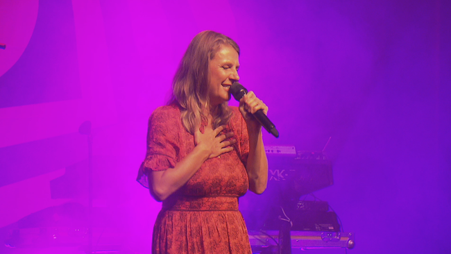 Nahaufnahme von Birgit Denk auf der Bühne, sie singt mit geschlossenen Augen und Hand auf der Brust gefühlvoll ins Mikrofon