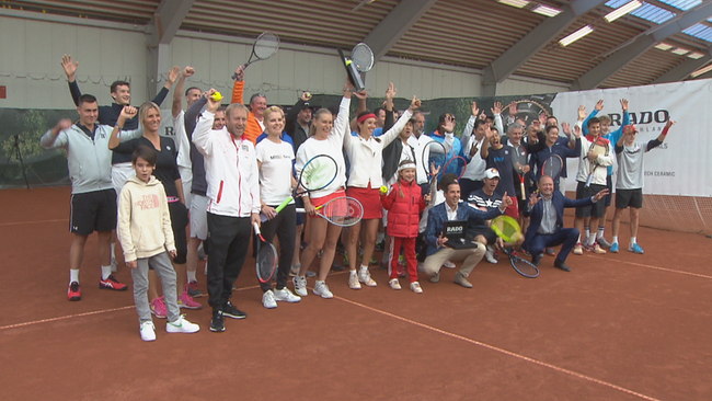Große Gruppe aus TennisspielerInnen, groß und klein, jubelt am Platz in die Kamera
