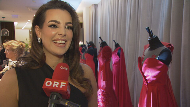 Nadine Mirada lachend im Interview, im Hintergrund die ausgestellten roten Kleider