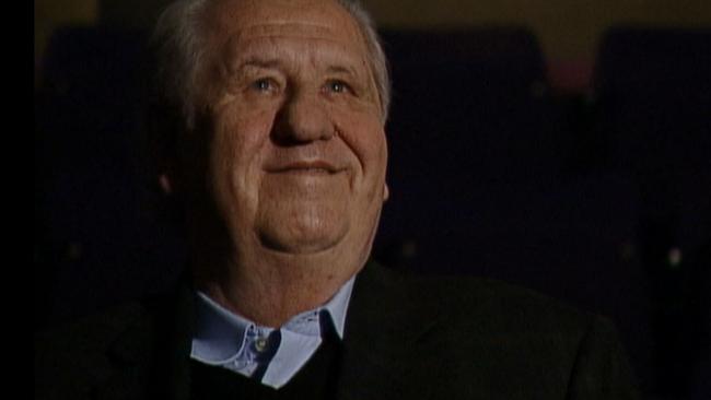 Karl Spiehs sitzt lächelnd alleine in einem dunklen Kinosaal, Blick auf die Leinwand