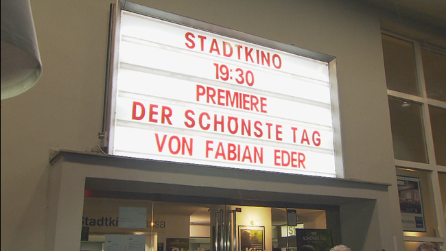 Leuchtschild vorm Kino auf dem steht: "Stadtkino, 19:30, Premiere, Der schönste Tag, von Fabian Eder"