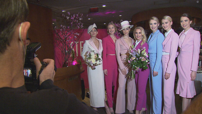 © ORF2/Seitenblicke Schneider in der Mitte in violettem Anzug mit großem Blumenstrauß, links und rechts von ihr die Models in bunten Smokings