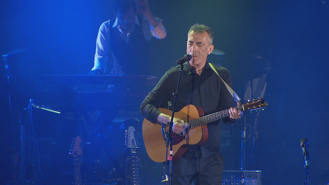 © ORF2/Seitenblicke Goisern mit geschlossenen Augen, singt, spielt Gitarre, blaues Licht und der Keyborder im Hintergrund