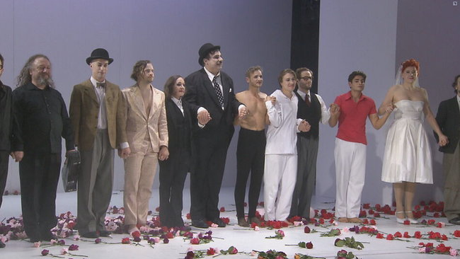 Schlussapplaus: Männer auf der Bühne in Anzügen und teilweise als Frauen, die Bühne ist mit rosa und roten Rosen bedeckt