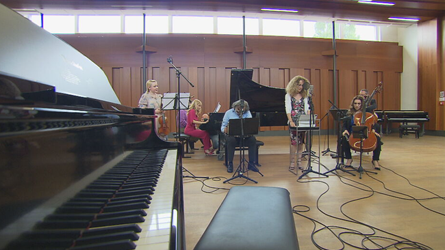 Links im Bild die Tastertur eines Klaviers, im Hintergrund zwei Sängerinnen, Angatscheva am Flügel, Ein Zieharmoniker-Spieler und eine Cellistin