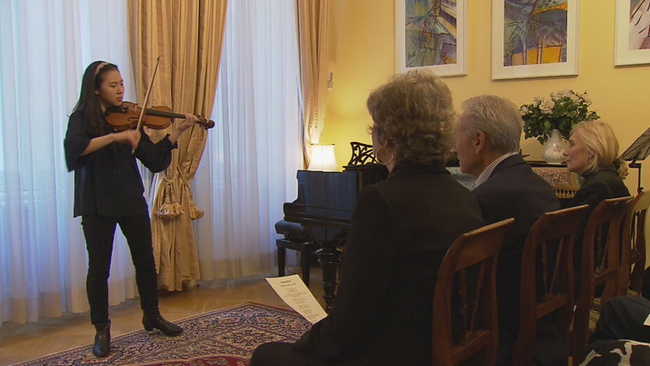 Violinistin spielt Geige in einem Wohnzimmer, in der ersten Reihe 3 Zuhörer*innen