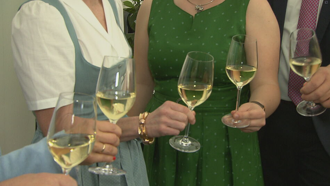 Fünf Weingläser in der Nahaufnahme, zwei gehalten von Frauen im Dirndl, die anderen beiden nicht sichtbar