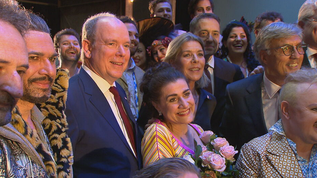 Bartoli posiert breit lächelnd mit Rosemstrauß zwischen Fürst und Prinzessin, um sie herum das Ensemble und MitarbeiterInnen