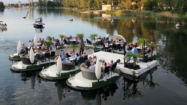 von der Brücke aus fotografiert auf die Alte Donau: schwimmende Floße mit Sesseln und Bühne