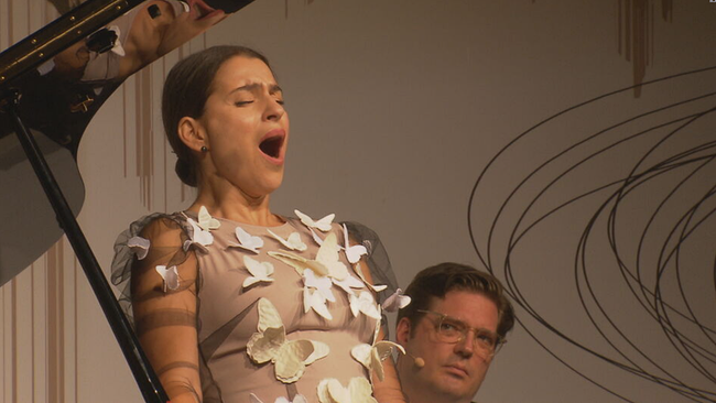 Asmik Grigorian singt mit weit geöffnetem Mund. Auf ihrem Kleid sind weiße Schmetterlinge aufgemalt