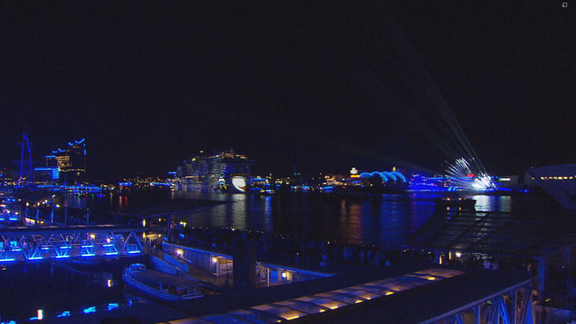 Der Hamburger Hafen mit vielen blauen Lichtern. Man sieht mehrer Schiffe, die ebenalls blau beleuchtet sind