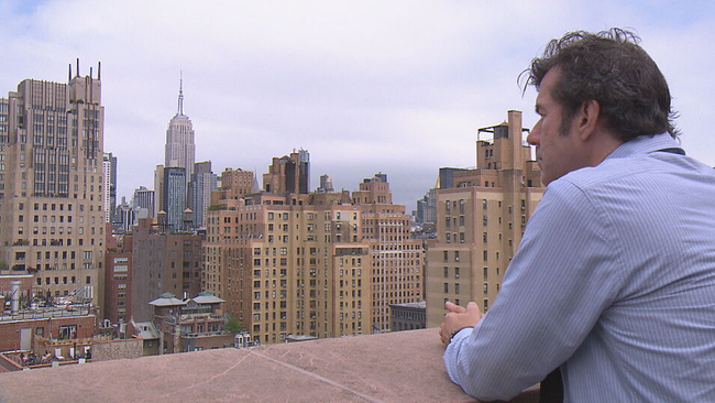Künstler Stefan Sagmeister steht auf einer Dachterasse in New York und blickt auf die Skyline 