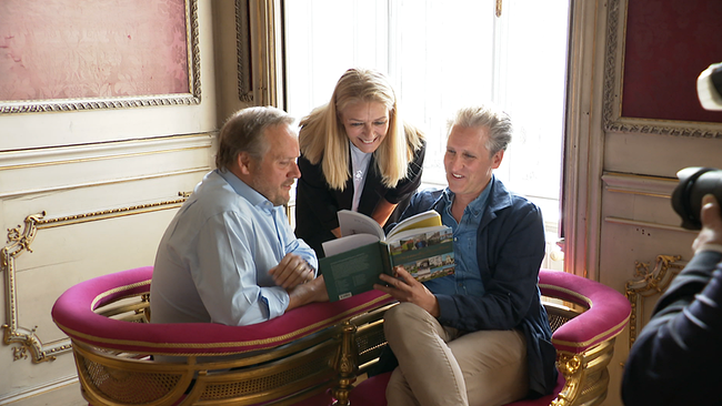 Zwei Männer und eine Dame betrachten gemeinsam ein Buch.