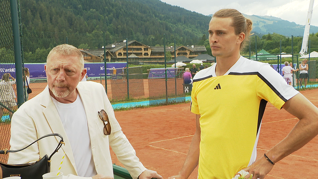 Ein mittelalter Mann und ein sportlicher junger Mann stehen auf einem Tennisplatz in den Bergen.