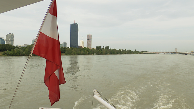 © ORF / Seitenblicke Am Heck eines Schiffes, das auf der Donau bei Wien unterwegs ist, ist eine österreichische Flagge zu sehen.