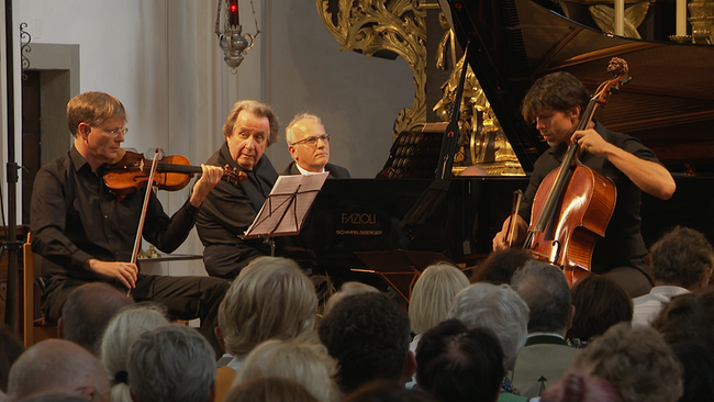 © ORF/ Seitenblicke Drei Männer spielen in einer Kirche vor Publikum auf klassischen Instrumenten.