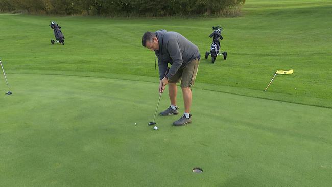 Ein Mann in einer eher unsportlichen Haltung versucht einen Golfball einzulochen.