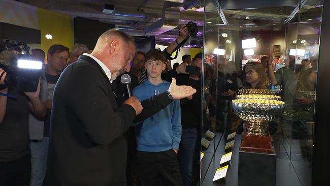 Ein Mann steht vor einer Vitrine und berichtet einer Menschenmenge von deren Inhalt.